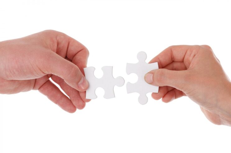 Twee handen die samen twee puzzelstukjes in elkaar steken