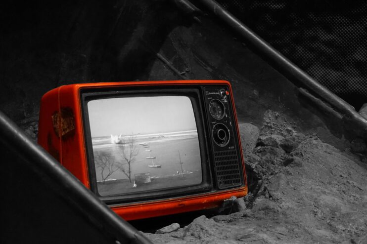 Oude rode televisie met zwart-wit beeld ligt in een bak met zand
