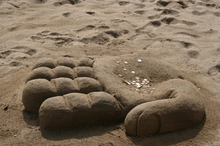 Een zandsculptuur in de vorm van een hand op het strand met wat muntgeld erin