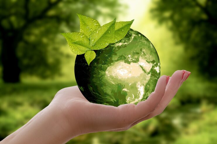 Een groene wereldbol wordt vastgehouden door een vrouwenhand met natuur op de achtergrond