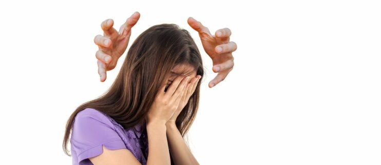 Een vrouw slaat haar handen voor haar gezicht terwijl grote mannenhanden boven haar hoofd zweven